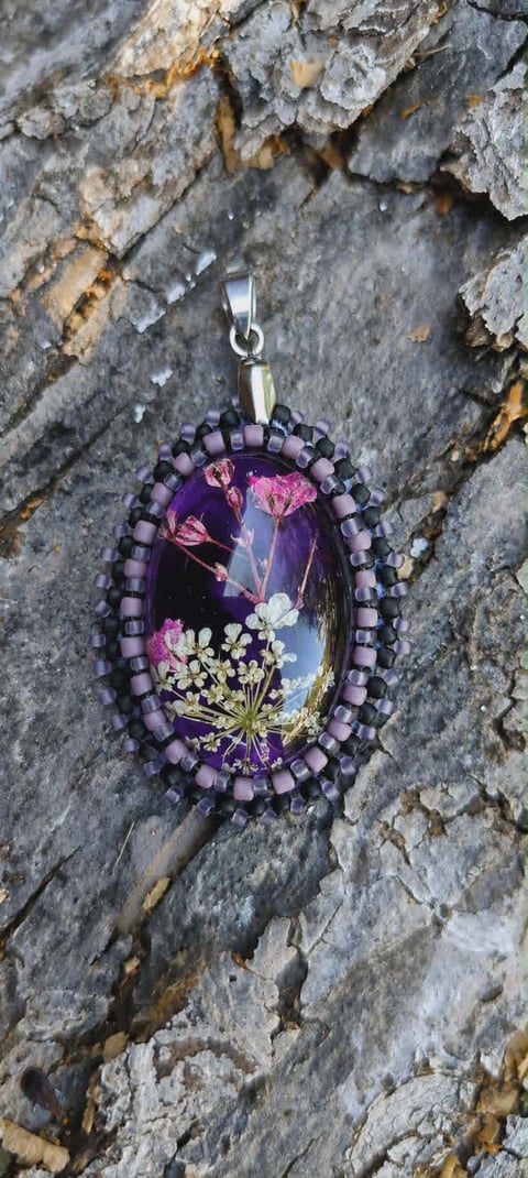 Handmade pendant with purple beaded border and dried flowers under resin on weathered stone background