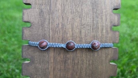 Blue beaded bracelet with three brown wooden beads on weathered wooden block with green grass background