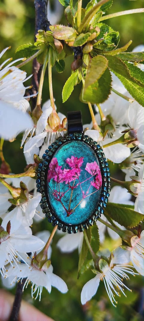 Decorative oval pendant with turquoise background and pink floral design, hanging among white flowering branches