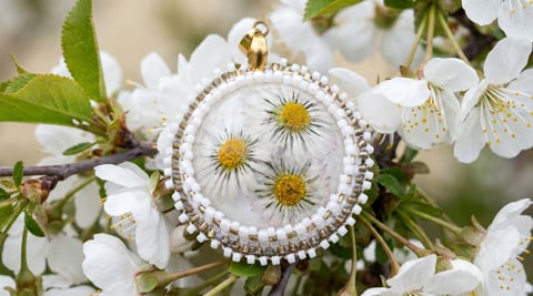 Pearl-bordered pendant with three yellow daisies displayed among white spring blossoms and green leaves