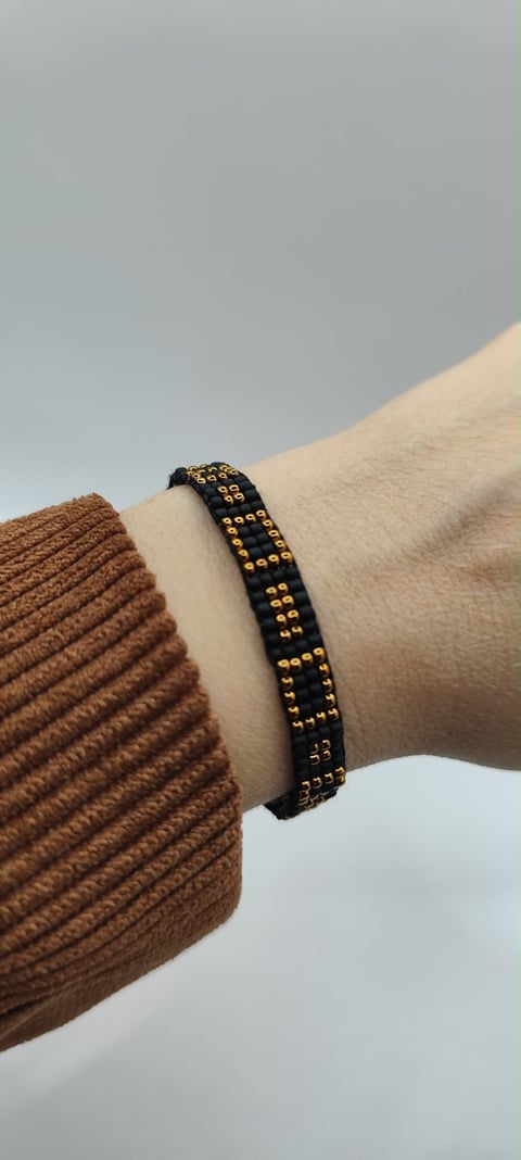 Black leather bracelet with gold studs worn on wrist over brown sweater