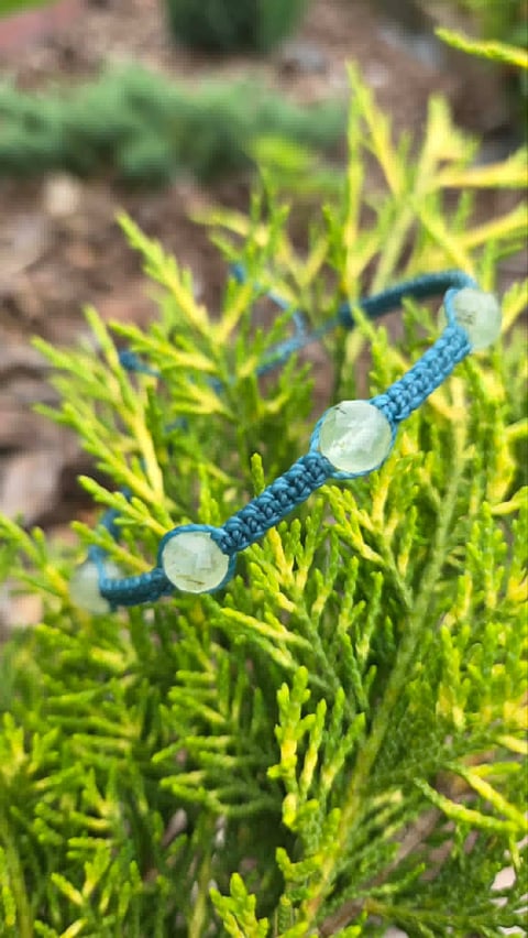 Blue beaded bracelet with white stone accents resting on bright green moss or plant foliage outdoors
