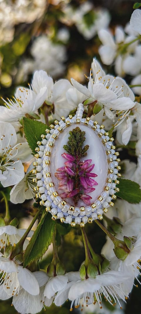 Oval-shaped ornament with pressed pink flower display surrounded by white blossoms with gold stamens