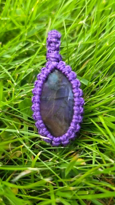 Purple beaded pendant with dark stone center displayed on bright green grass