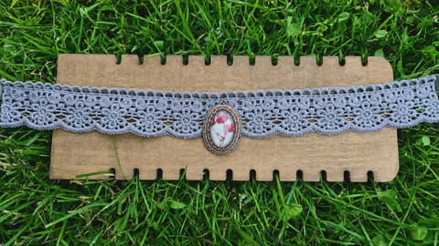 Handmade bracelet with gray lace ribbon and vintage cameo charm on cardboard display card over green grass