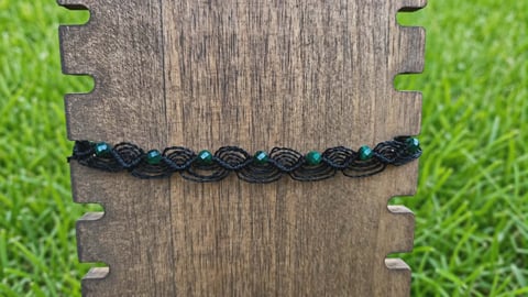 Braided black and teal cord bracelet on wooden board with metal accents and green grass background
