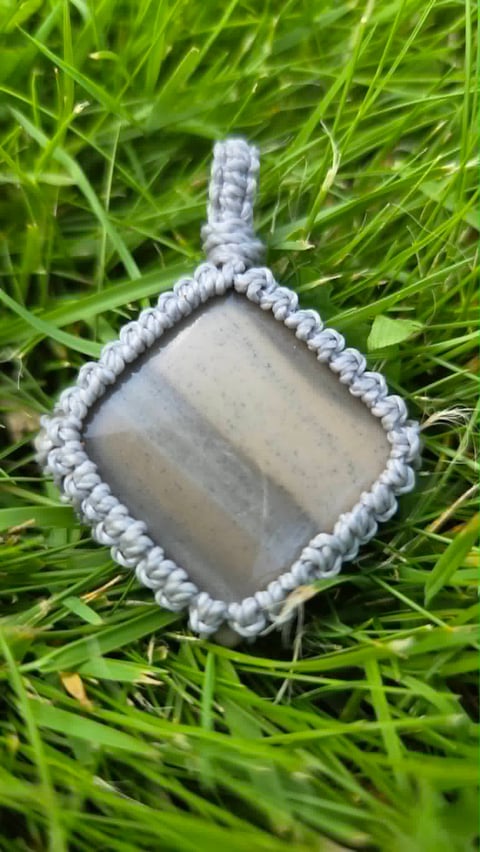 Square stone pendant with gray braided rope border displayed on green grass