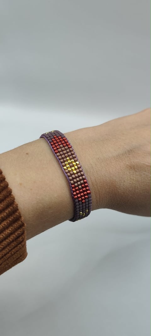 Beaded bracelet with gradient colors from purple to yellow on wrist against cloudy sky background