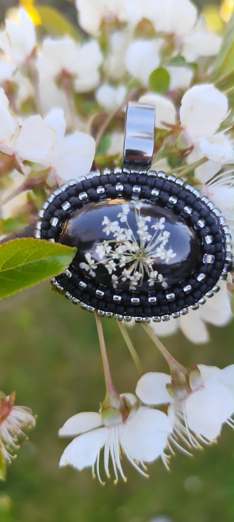 Black ornamental pendant with rhinestone border and dried flower encasement, hung on white flowers with green foliage