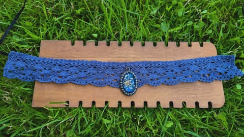 Blue lace choker necklace with turquoise gem on wooden display stand on grass